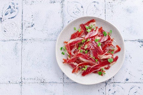 Ham of duck breast, dried duck fillet, with microgreens, plate, on a tiled table