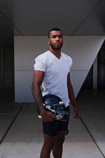 A confident American football player stands in a white jersey, holding a helmet, ready for the game