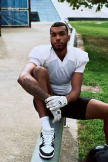 A young American football player in a white jersey sits on a bench outdoors, exuding confidence and