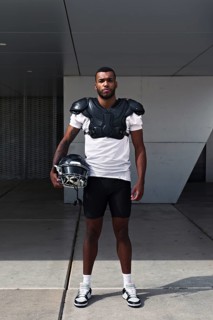 A determined American football player stands confidently, wearing shoulder pads and holding a