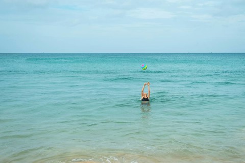 A young woman engaged in playful activity with a colorful ball in the calm ocean water in Thailand,
