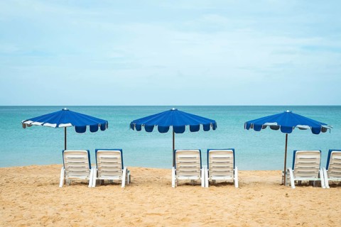 A serene beach scene with three blue umbrellas and white lounge chairs on golden sand facing a
