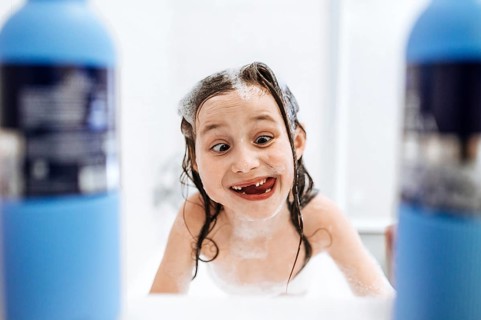 A joyful child enjoys bath time, playfully covered in foam and surrounded by bubbles, exuding