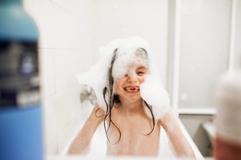 A joyful child enjoys a playful bath, covered in foamy soap bubbles, smiling widely. The bright