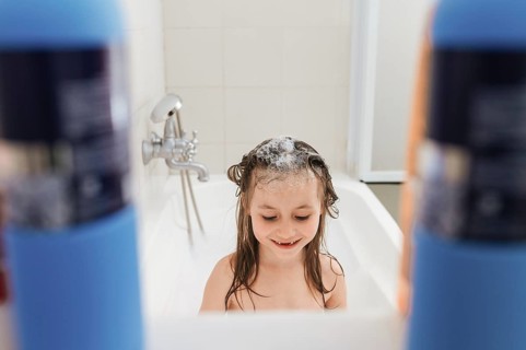 A joyful child enjoys a bath, crowned with soap bubbles. Surrounded by shampoo bottles, the playful