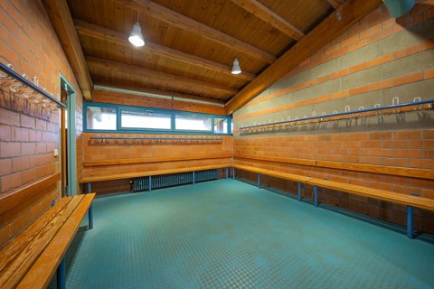 Spacious changing room with wooden ceiling and brick walls as well as benches and bright lamps,