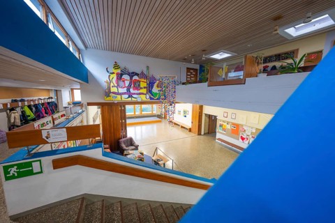 An interior with a staircase, decorated with art and a pleasantly illuminated wooden ceiling,