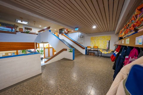 A bright corridor with cloakroom, colorful wall art and a modern wooden staircase, Schlehengäu