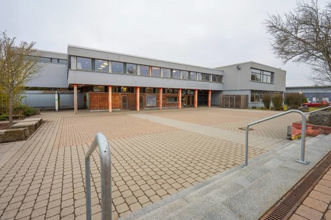 A schoolyard with extensive pavement, gray building structure and outdoor tree, Schlehengäu Grund