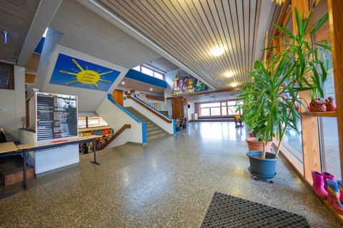 A corridor with stairs, decorated with plants and works of art, wooden ceiling, well-lit,