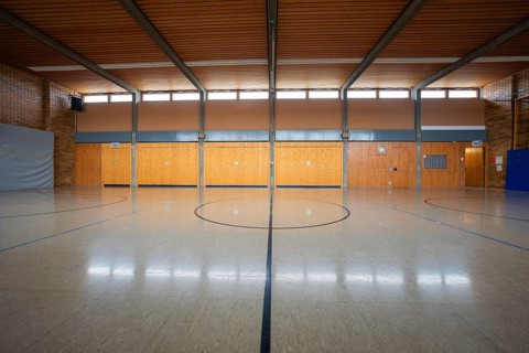 Large sports hall with wooden elements and a central playing field marker, Schlehengäu Grund Schule