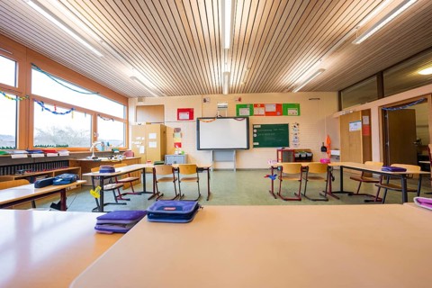 Empty classroom with a view of seating arrangements and blackboards, well-lit through large