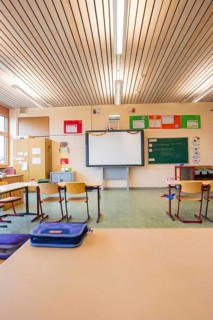 Classroom with wooden furniture and blackboard under an illuminated wooden ceiling, Schlehengäu