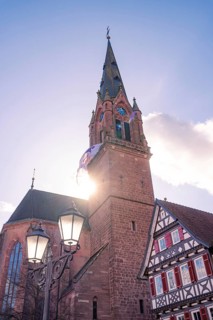 Church tower in sunlight next to a traditional half-timbered house under a clear sky, Calw, Calw