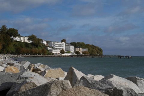 Large stones on the shore, behind Hotel Fürstenhof and pier, blue sky and clouds, Sassnitz, Rügen,