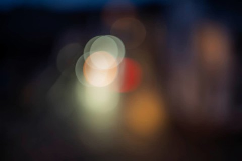 Colourful lights illuminate the city street at night. The scenes are blurred and there is movement.