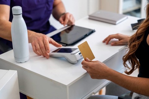 Patient making a contactless payment with a gold credit card on a pos terminal at a medical clinic