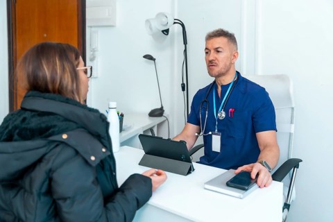 Healthcare professional wearing blue scrubs and a stethoscope talking with a female patient,