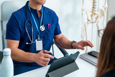 Doctor in scrubs discussing health information with patient, using a tablet for digital records