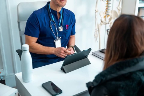 Healthcare professional reviews digital records on a tablet while consulting with a patient in a