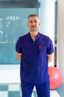 Professional physiotherapist wearing a purple scrub uniform is standing confidently in a modern
