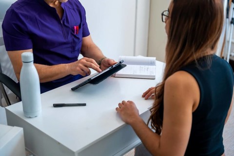 Professional osteopath or physiotherapist doctor in medical scrubs consulting a female patient,