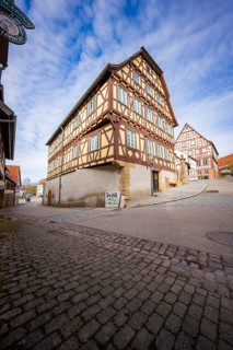 Two large half-timbered houses with red and white details on a busy street corner, Ötisheim,