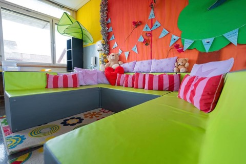 Cosy seating area with colorful pillows and cuddly toys, decorative background, homework