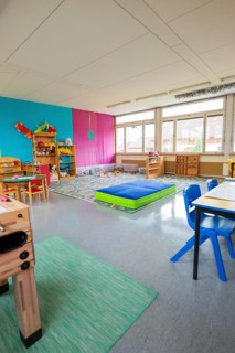 Bright kindergarten room with colorful walls and toy shelves, daylight through large windows,