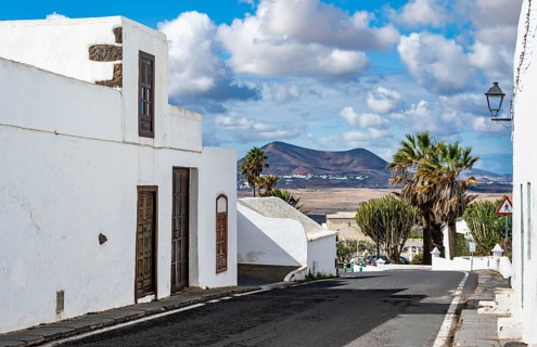 Typical white houses with colored doors and windows in an alley with volcanic craters behind,