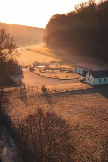 Sewage treatment plant at sunrise in a meadow with long shade, surrounded by trees and fog,