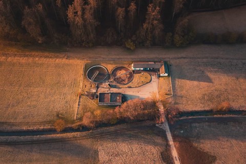 Sewage treatment plant with round basins and buildings in the midst of a wide field landscape with