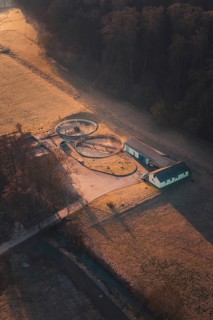 Sewage treatment plant surrounded by fields and trees, illuminated by the morning sun with long