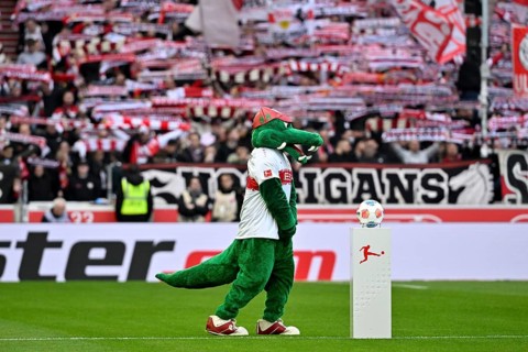 Mascot Fritzle VfB Stuttgart in front of Adidas Derbystar match ball on podium, behind fan block,