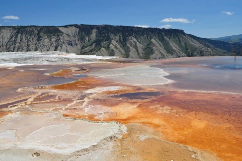 Hot springs with orange and white deposits against mountain backdrop, Yellowstone National Park,