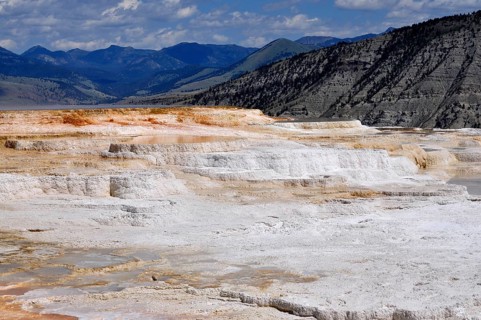 Limestone terraces against mountain backdrop under cloudy sky, Yellowstone National Park, Wyoming,