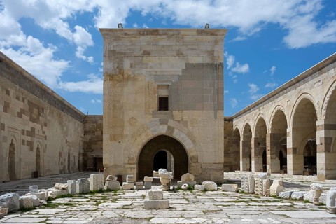 Old courtyard with stone arches and scattered ruins under a clear sky, Sultanhani caravanserai, on