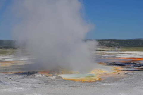 Colorful hot spring with steam under clear skies in a vast natural landscape, Yellowstone National