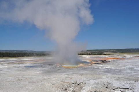 A hot spring with rising steam in an open landscape under clear skies, Yellowstone National Park,