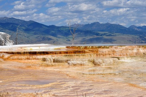 Wide views of hot springs with mountains in the background under cloudy sky, Yellowstone National