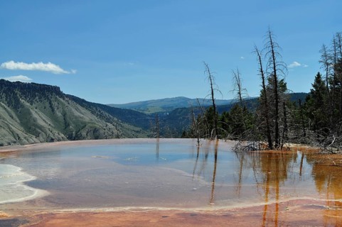 Natural pool with volcanic deposits and reflections and extensive views of mountains, Yellowstone