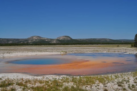 An orange geothermally active area in front of a mountainous landscape, Yellowstone National Park,