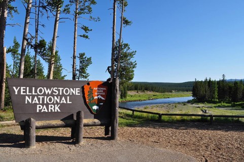 Yellowstone National Park entrance sign with trees and a river in the background, Yellowstone