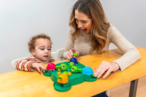 Happy mother and toddler play a colorful tabletop turtle game, smiling and learning together while
