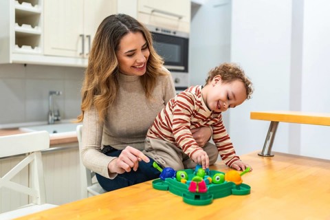 Happy mother and her toddler son enjoying a fun board game together at the kitchen table, sharing
