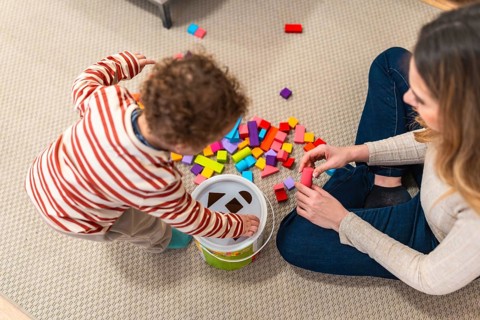 Parent and toddler bonding on the living room floor, engaging in educational play with a shape