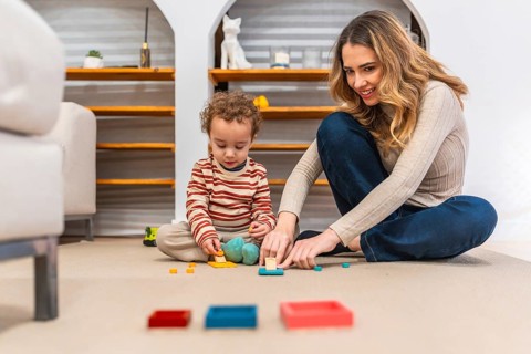 Young mother happily interacting with her toddler son, both sitting on a carpeted floor, engrossed