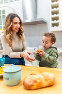 Mother looking at her happy child holding a muffin while having breakfast in a home kitchen,
