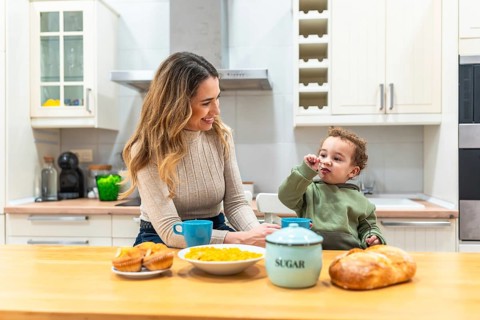Mother smiles at her young child across the kitchen counter during a bright, cozy breakfast,