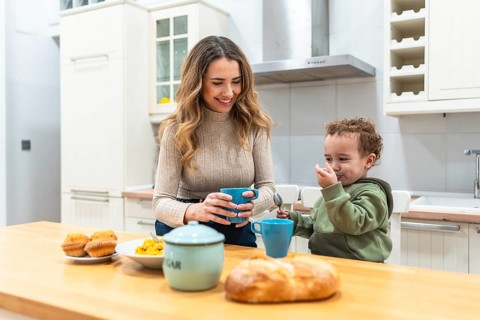 Mother and toddler share a warm morning at the kitchen counter, woman smiling with a mug while the